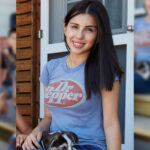teenage girl wearing a shirt with the Dr Pepper logo sits on a porch with a small dog in her lap.