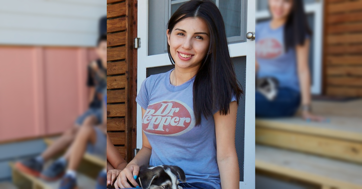 teenage girl wearing a shirt with the Dr Pepper logo sits on a porch with a small dog in her lap.