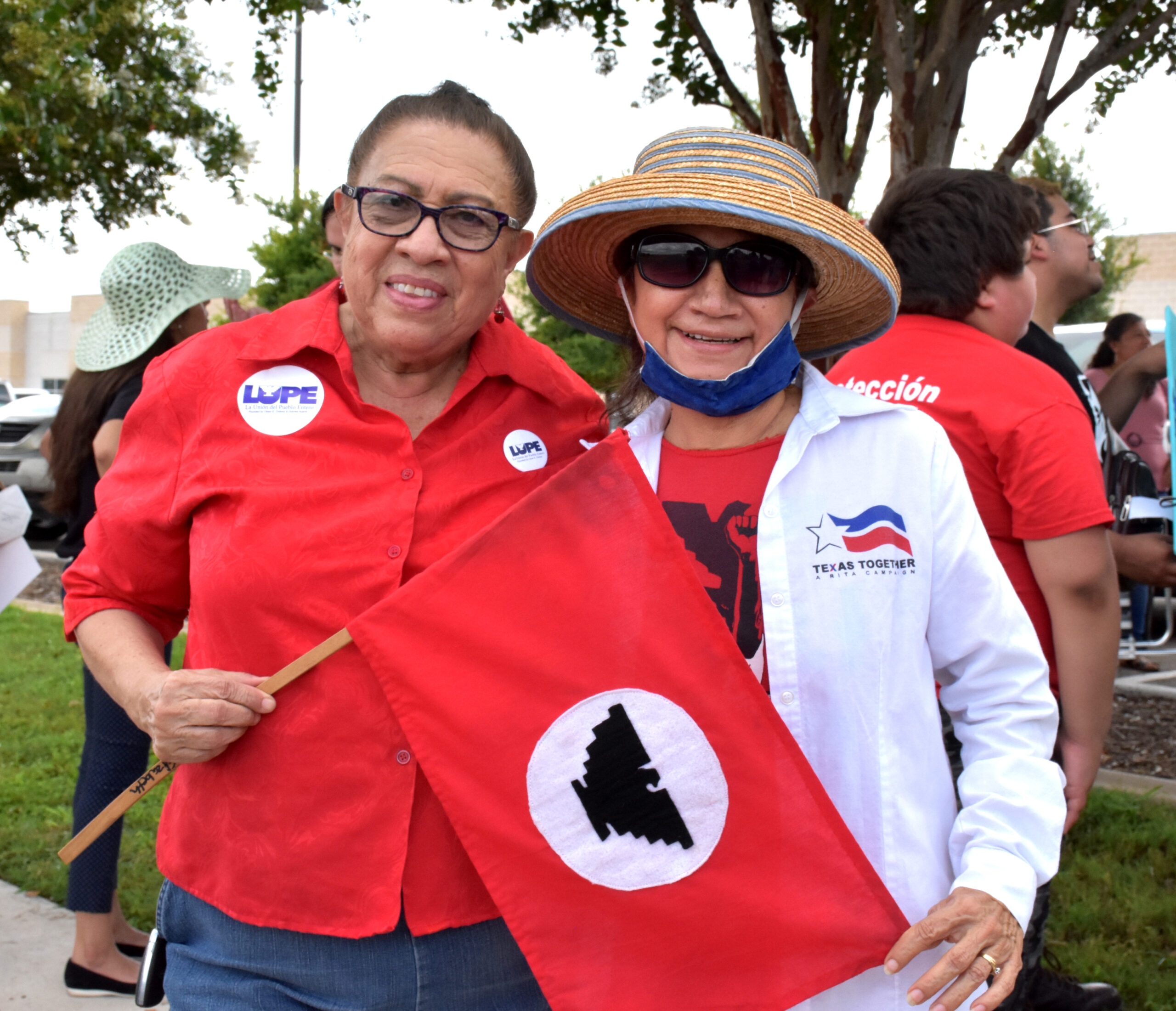 Juanita stands next to Martha, together they hold a red and black UFW union flag
