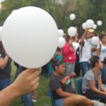 Young people gathered together hold white balloons at an outside event