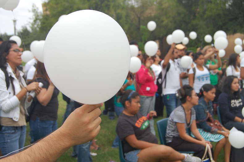 Young people gathered together hold white balloons at an outside event