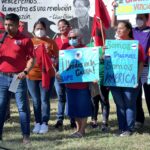 Immigrant youth speaks on microphone in front of a line of protesters wearing red t-shirts and holding colorful signs